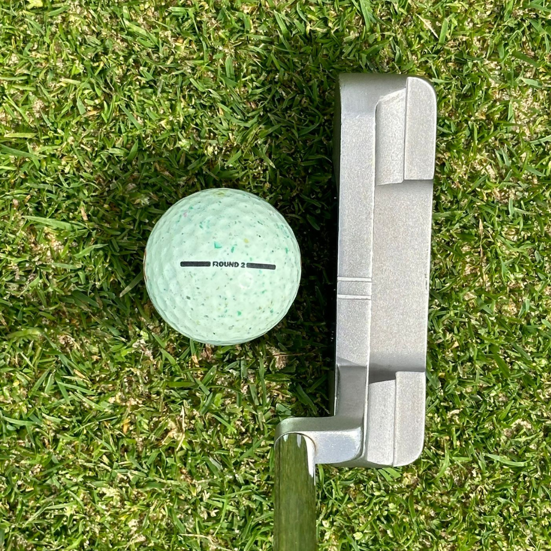 ROUND2 golf ball with alignment lines next to putter on green grass, ideal for new golfers, juniors, and high handicappers.